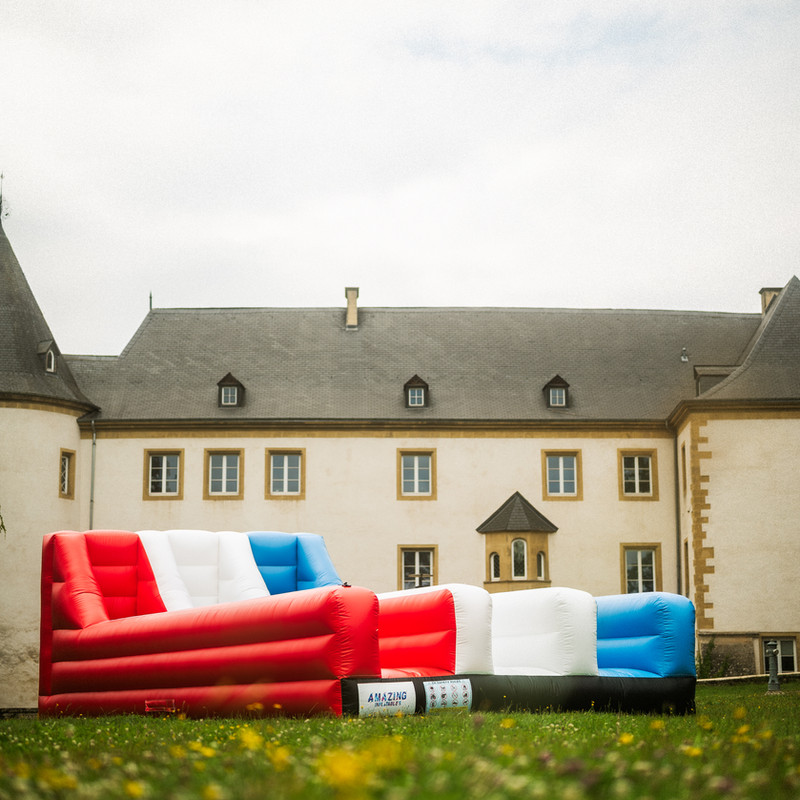 Piste gonflable Bungeerun bleu blanc rouge devant un château luxembourgeois.