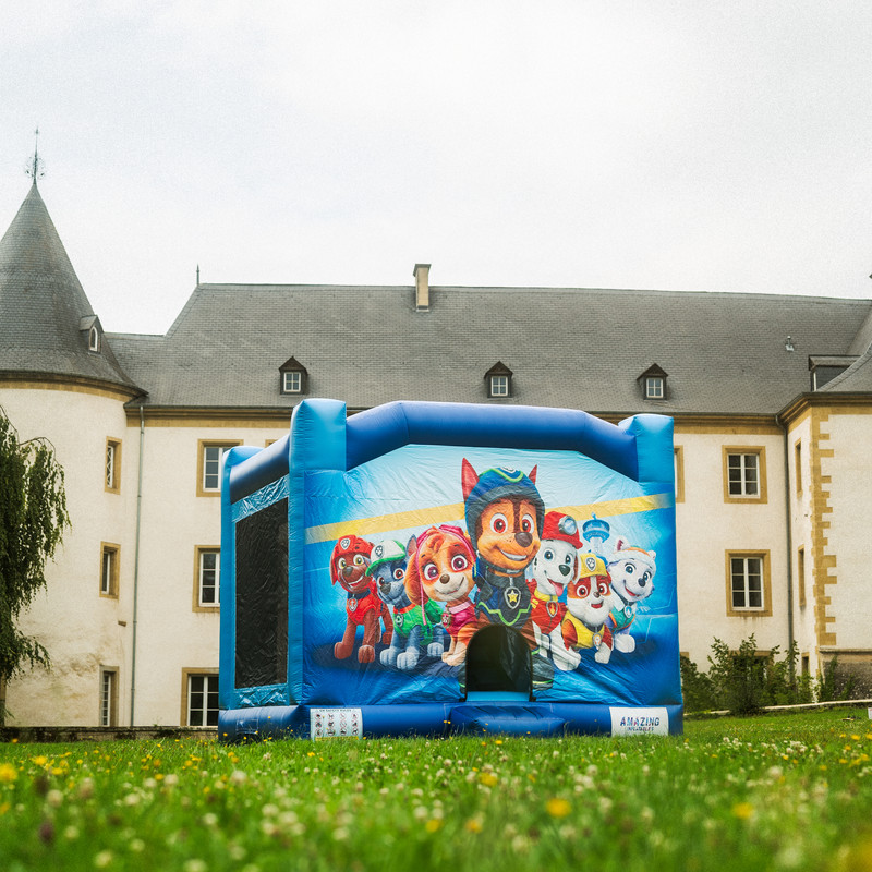Château gonflable Paw Patrol bleu avec Chase et Skye devant un château luxembourgeois.