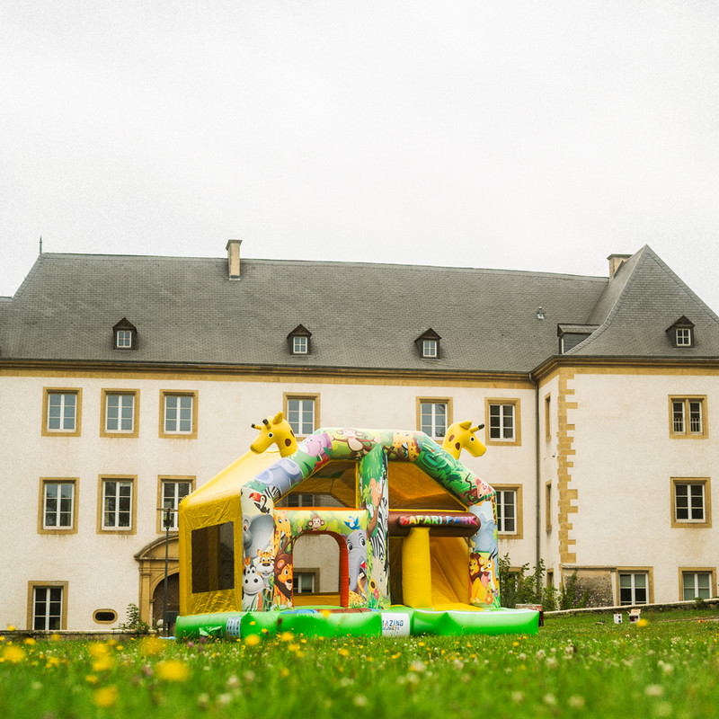 Château gonflable Safari Park avec girafes et animaux de la savane devant un château luxembourgeois.