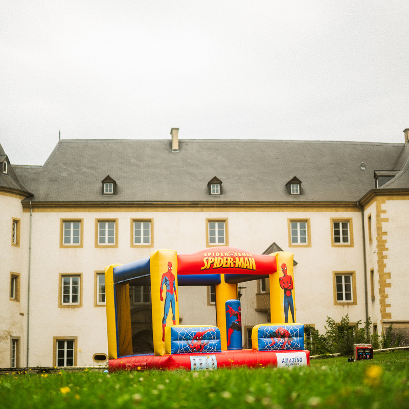 Château gonflable Spiderman rouge et jaune devant un château luxembourgeois.