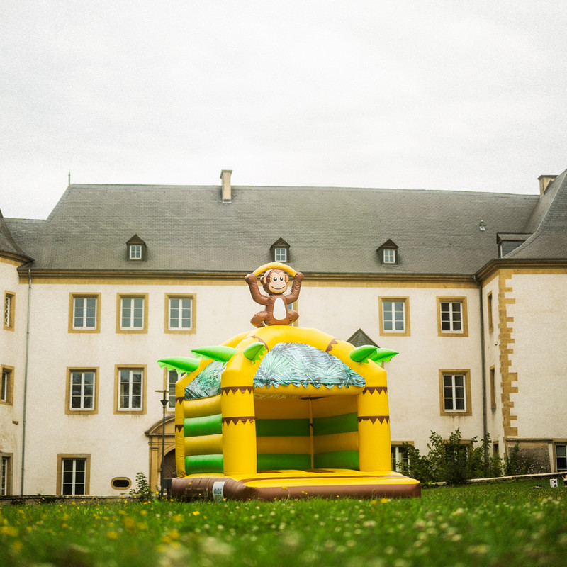 Château gonflable Monkey jaune décoré de singes devant un château luxembourgeois.