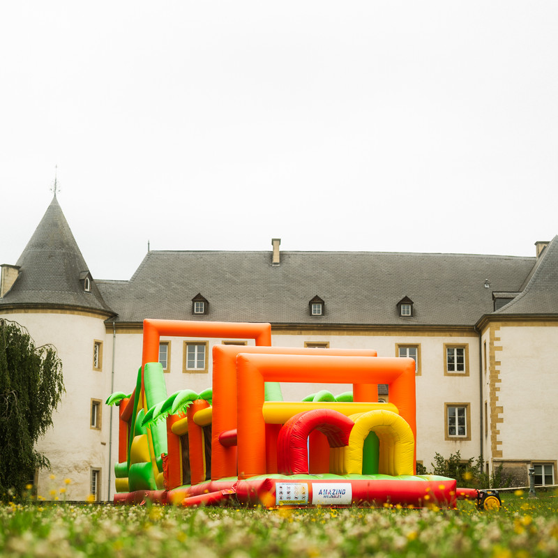 Grand parcours gonflable orange, jaune et vert avec obstacles devant un château luxembourgeois.