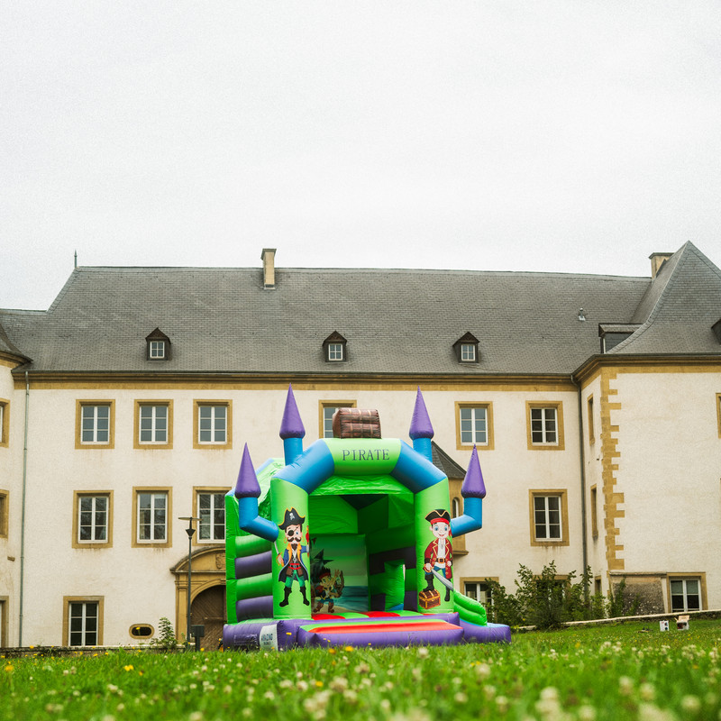 Château gonflable Pirate vert et violet avec tours et voiles devant un château luxembourgeois.